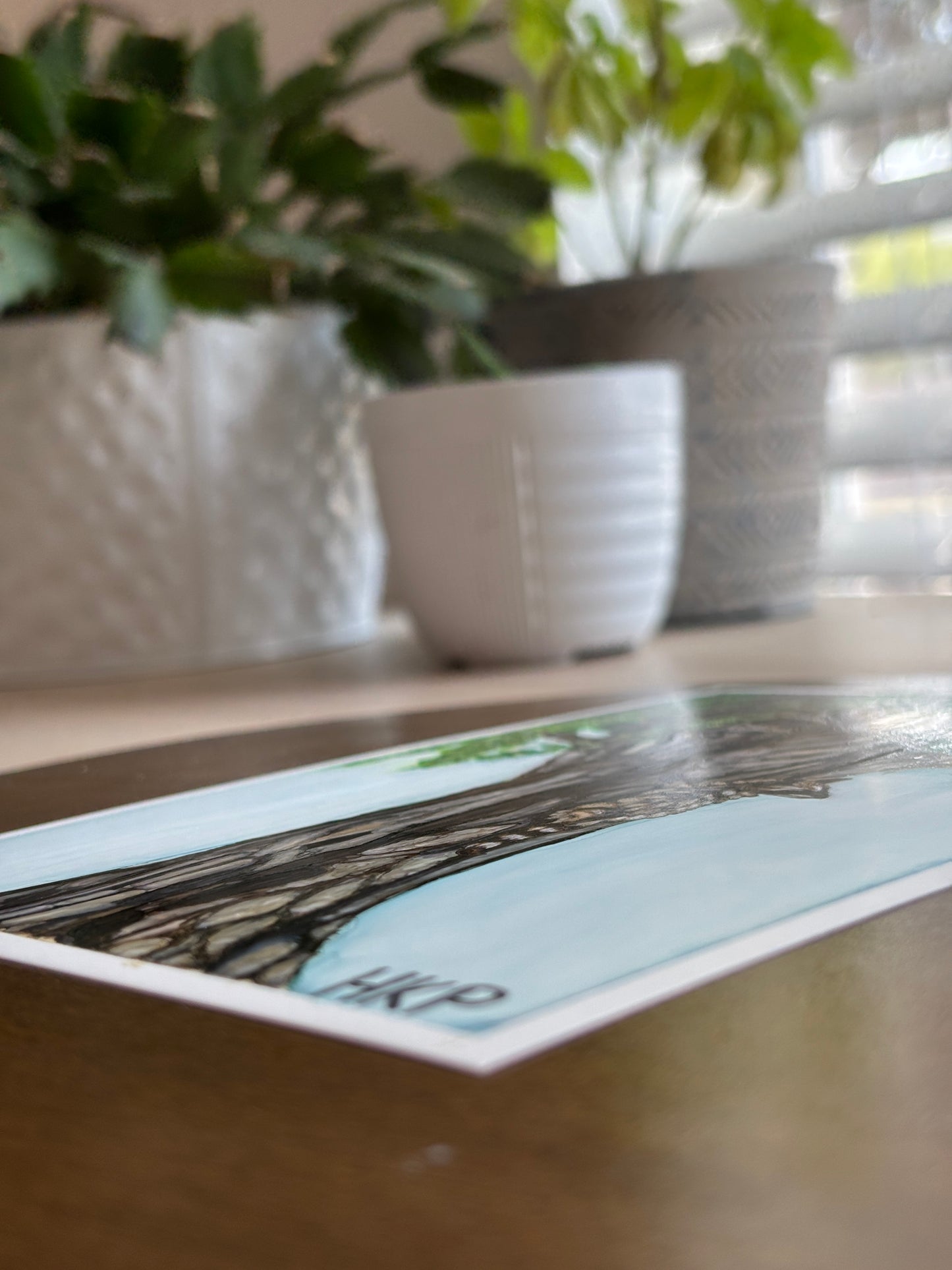 shot from the side of the painting of two young raccoons climbing a tree, showing that the painting is on a flat piece of paper